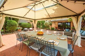 An outdoor dining area with a table set for four, surrounded by chairs, under a large umbrella.