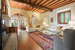 Un vaste salon doté d’un haut plafond, de poutres apparentes, d’une grande fenêtre avec des volets en bois et d’un tapis à motifs.