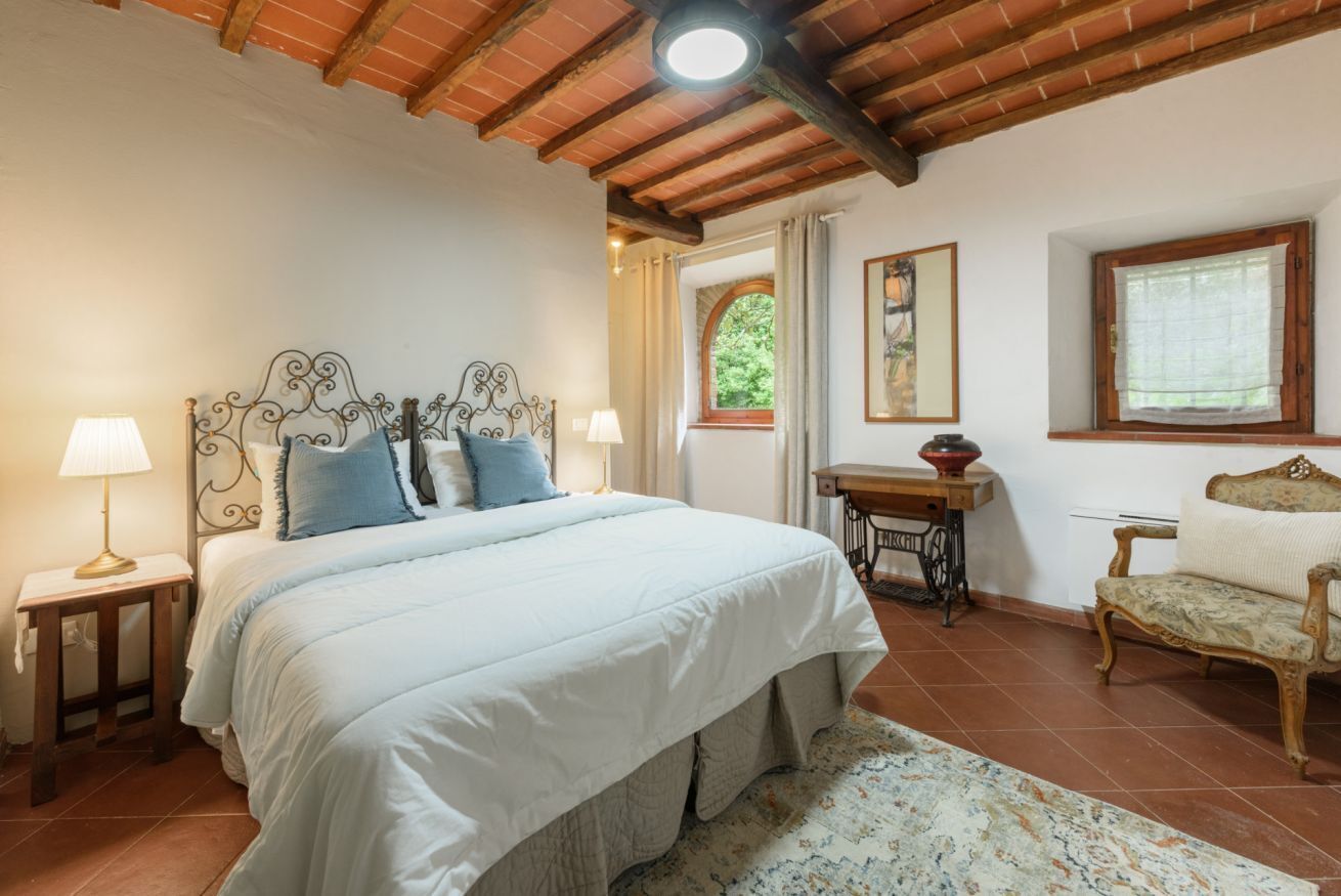 Ein Schlafzimmer mit einem Bett, Nachttischlampen, einem Holztisch, einem Stuhl und einem Fenster mit Vorhängen.