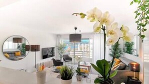 Een moderne woonkamer met een witte bank, een ronde spiegel en potplanten op een witte salontafel.