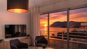 Een moderne kamer met een televisie, twee stoelen, een salontafel en een groot raam met uitzicht op een zonsondergang.