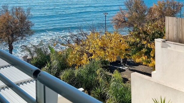 Een balkon met uitzicht op zee, een houten omheining en enkele planten.
