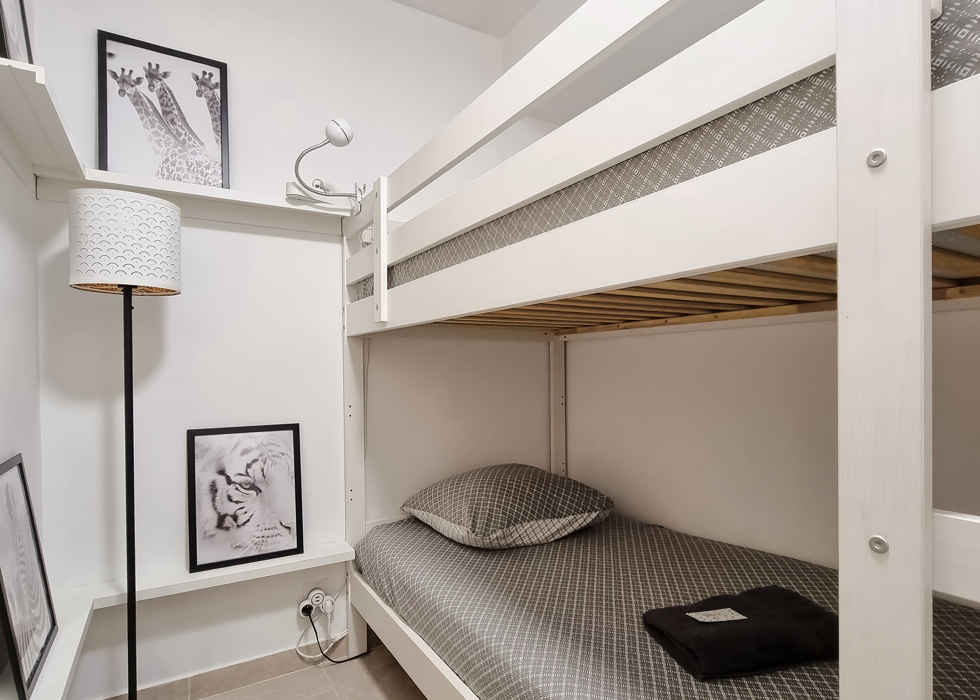 Habitación con literas, un cuadro de jirafa enmarco, una lámpara de pie y un cuadro abstracto enmarcado.