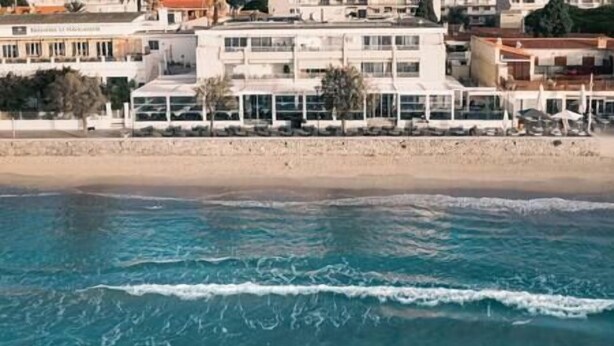 Hotel a la costa amb vistes a la platja, amb múltiples balcons i una platja de sorra al fons.