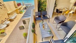 Ein Balkon mit Meerblick, möbliert mit Stühlen und Tischen, und mit Topfpflanzen.