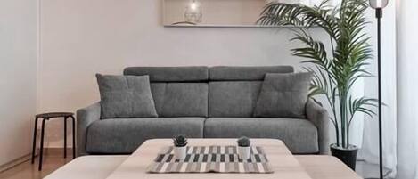 Ein modernes Wohnzimmer mit einem grauen Sofa, einem kleinen Tisch mit Schachbrett und einer hohen Stehlampe.