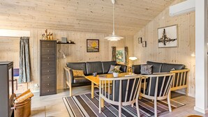 A cozy living room with a wooden ceiling, a sofa, a dining table with chairs, and a fireplace. - Stunning home in Tranekær with sauna (Tranekær)