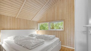 Un dormitorio con techo de madera, una cama grande y una ventana con vistas a follaje.