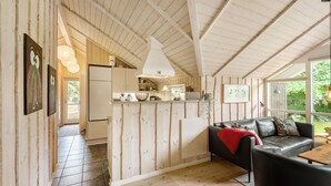 Acogedor interior de cabaña con paredes de madera, zona de cocina y espacio de estar con sofá y mesa.