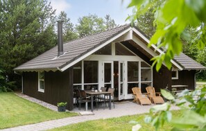 Une cabane en bois dotée d’un toit à pente, de grandes fenêtres et d’un espace patio avec des sièges d’extérieur.