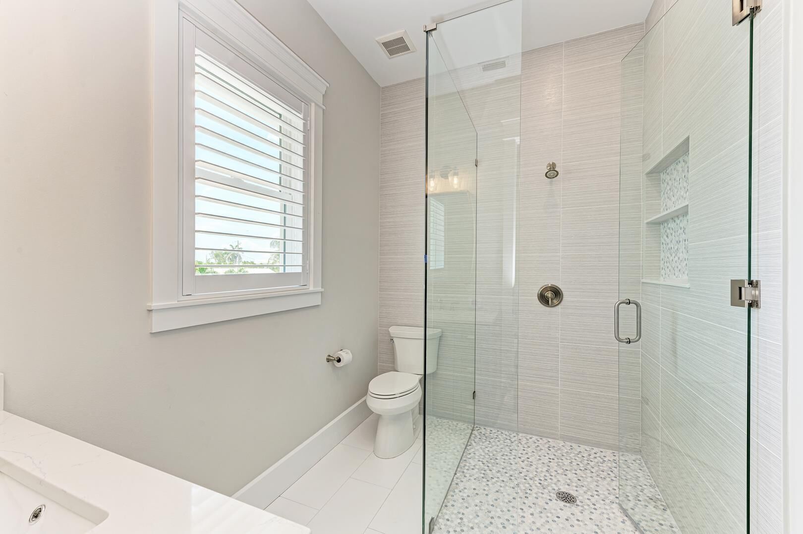 Une salle de bain moderne avec une douche à parois de verre, des toilettes et une fenêtre équipée de stores.