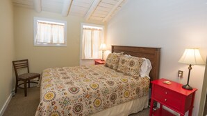 Una camera da letto con un letto, due comodini, una sedia e due finestre con tende.