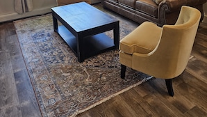 Un salón con un sofá de cuero marrón, un sillón amarillo, una mesa de centro negra y una alfombra estampada.