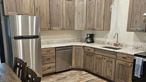 Una cocina con armarios de madera, un refrigerador de acero inoxidable, un lavavajillas y una encimera de granito.