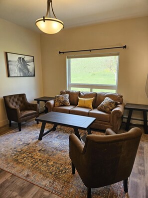 Relax in this serene space with a view of the surrounding green landscape, featuring a comfortable sofa and armchair.