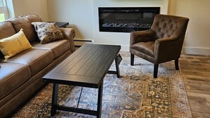 Un salon avec un canapé en cuir marron, un fauteuil marron, une table basse en bois, un tapis à motifs et un téléviseur à écran plat fixé au mur.