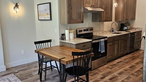 A modern kitchen with wooden cabinets, stainless steel appliances, and a dining area with a wooden table and chairs. - Your Ideal Retreat! Onsite Parking, Near Gardiner Downtown! (Gardiner)