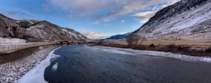 A river flowing through a mountainous landscape with snow-covered banks and a bridge on the left.