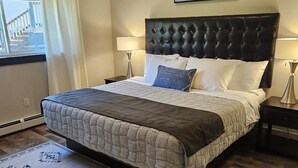 A bedroom with a large bed, two bedside tables with lamps, a window with curtains, and a painting on the wall.