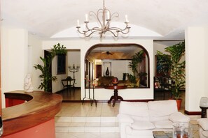 A spacious living area with a wooden reception desk, a white sofa, and a chandelier. - Nesthost Hotel Los Robles (Managua)