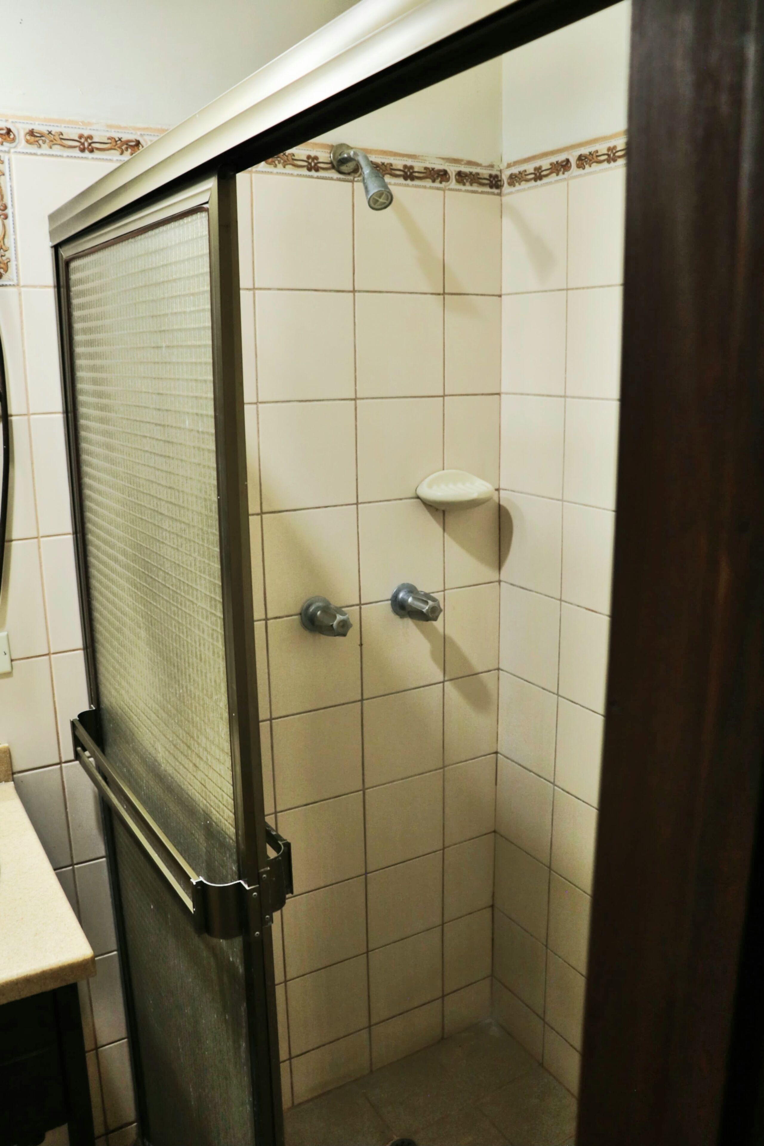 A small, tiled shower stall with a glass door, a soap dish, and a showerhead.