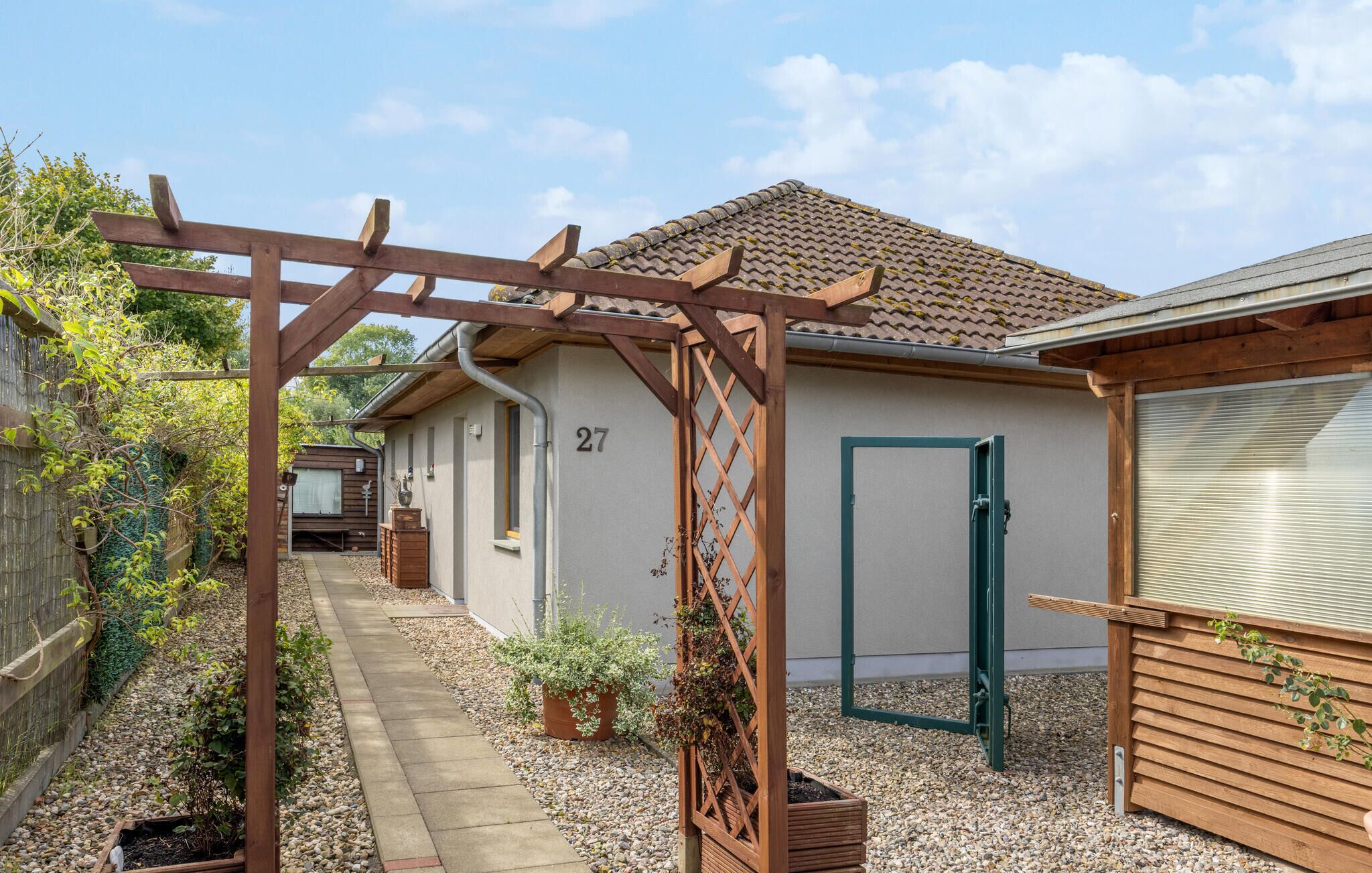 Il s’agit d’une propriété résidentielle portant le numéro 27, dotée d’une pergola en bois, d’un chemin de jardin et d’une maison avec un toit en tuiles.