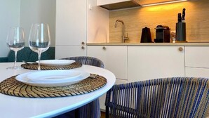 A modern kitchen with white cabinets, a wooden backsplash, and a dining area with a table set for two. - Enchantment (Monopoli)