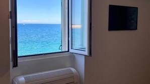 A room with a large window overlooking the sea, a white radiator, and a flat-screen TV mounted on the wall. - Enchantment (Monopoli)