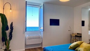 A bedroom with a bed, a window with a view of the sea, a potted plant, and a wall-mounted air conditioner. - Enchantment (Monopoli)