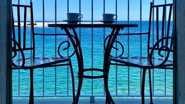 A balcony with a table and two chairs, overlooking a turquoise sea. - Enchantment (Monopoli)