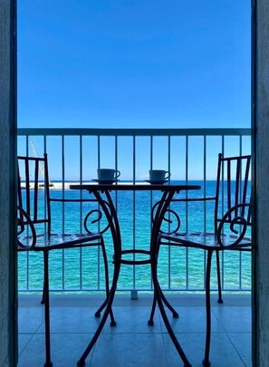 A balcony with a table and two chairs, overlooking a turquoise sea. - Enchantment (Monopoli)