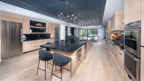 A modern kitchen with a large island, stainless steel appliances, and a dark ceiling.