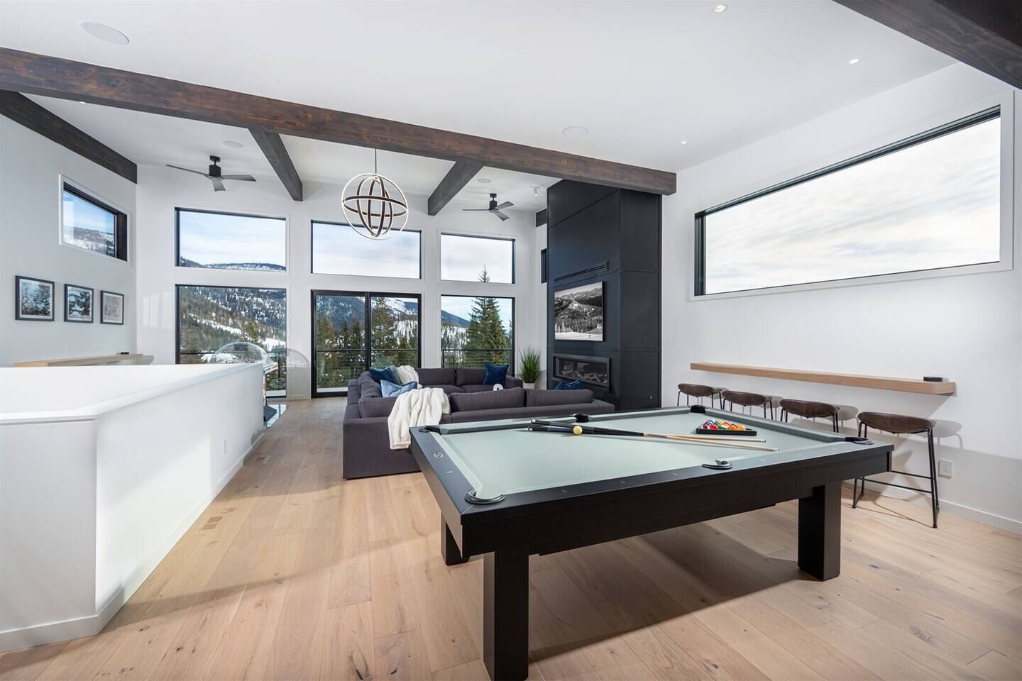 A modern living room with a pool table, a sofa, and a balcony with a view of mountains.