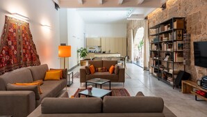A modern living room with a sofa, coffee table, and bookshelf. There is a kitchen in the background. - Valverde Art Space by DomuSicily (Palermo)