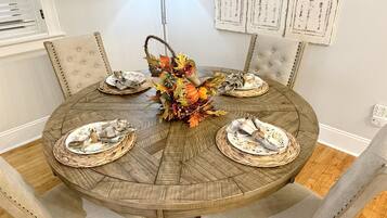 Une table de salle à manger ronde en bois, accompagnée de quatre chaises, d’un set de table en fibres naturelles et d’un centre de table décoré de feuilles d’automne.