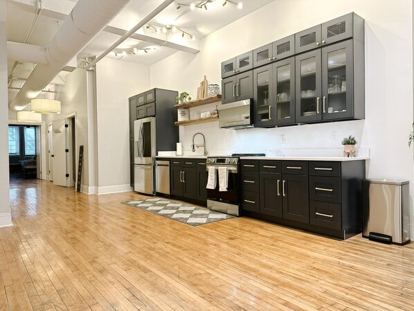 A modern kitchen with dark cabinetry, stainless steel appliances, and a wooden floor. - The Historic Lyric Presidential Suite (Cincinnati)