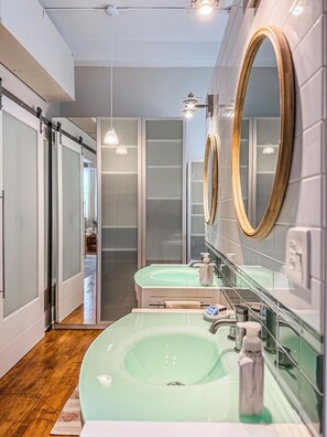 A modern bathroom with two sinks, frosted glass doors, and a wooden floor. - The Historic Lyric Presidential Suite (Cincinnati)