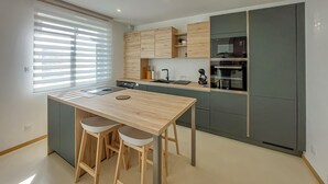 Una cocina moderna con una isla central, taburetes de bar, electrodomésticos integrados y un ventanal con persianas.