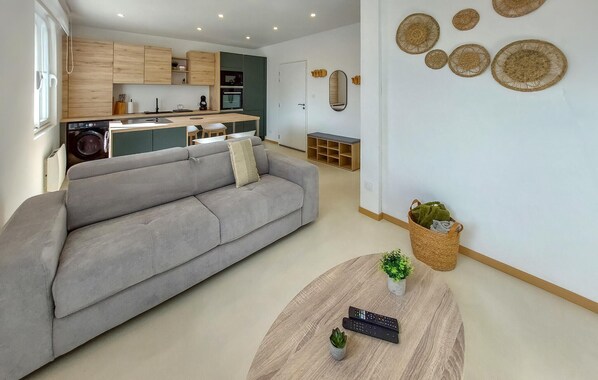 A modern living room with a grey sofa, a round coffee table with remote controls, and a kitchen in the background. - Beautiful apartment in Le Conquet with WiFi (Le Conquet)