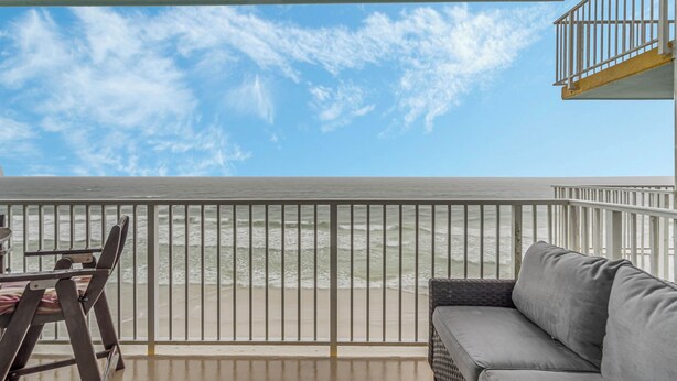 A balcony with a view of the ocean, a wicker sofa, and a table with chairs.
