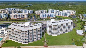A high-rise hotel with multiple balconies, a parking lot, and a view of a coastal area with water bodies.
