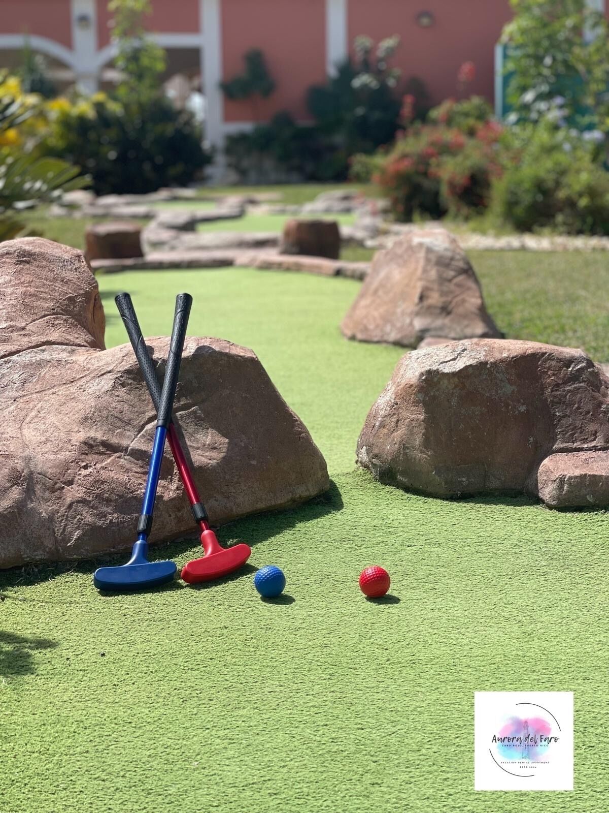 Un parcours de mini-golf avec deux putters et deux balles de golf sur un gazon synthétique, entouré de gros rochers.