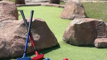 Un parcours de mini-golf avec deux putters et deux balles de golf sur un gazon synthétique, entouré de gros rochers.