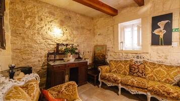 A stone-walled room with a wooden ceiling, a sofa, a small table with a vase, and a window with an exit sign.
