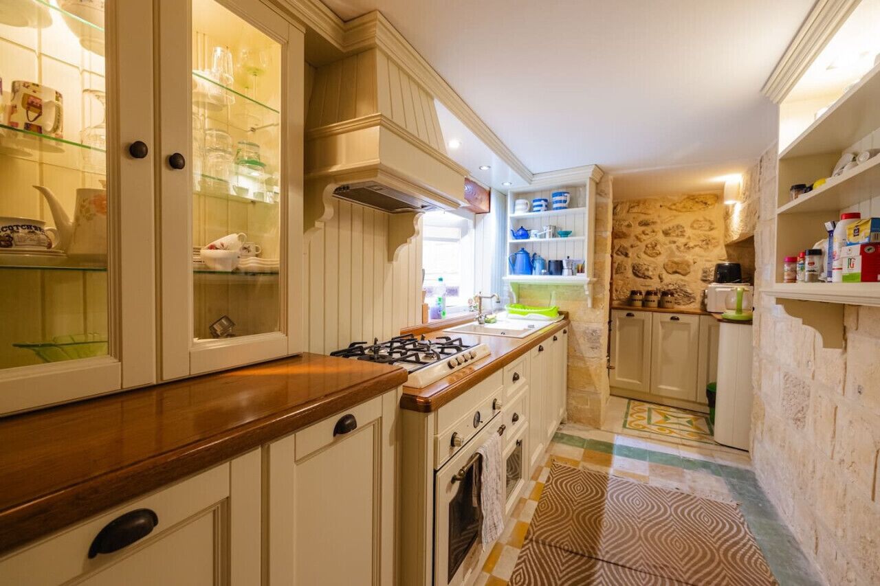 A kitchen with white cabinetry, a gas stove, and a stone wall.
