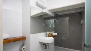 Une salle de bain moderne avec un lavabo blanc, un miroir, des toilettes et un espace douche.