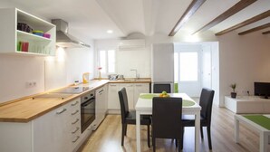 A modern kitchen with white cabinets, a wooden countertop, and a dining area with a white table and black chairs. - SingularStays Cervantes I (València)