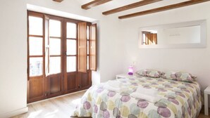 A bedroom with a large window, wooden beams on the ceiling, a bed with a colorful duvet, and a bedside table with a lamp. - SingularStays Cervantes I (València)