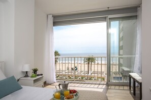 Un balcon avec vue sur la plage, un plateau de petit-déjeuner avec des fruits et du jus, et un lit avec un oreiller et une table de chevet avec une lampe et une plante.