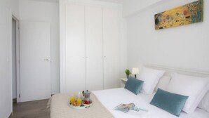 A bedroom with a bed, a bedside table with a lamp, a tray of breakfast, and a painting on the wall.